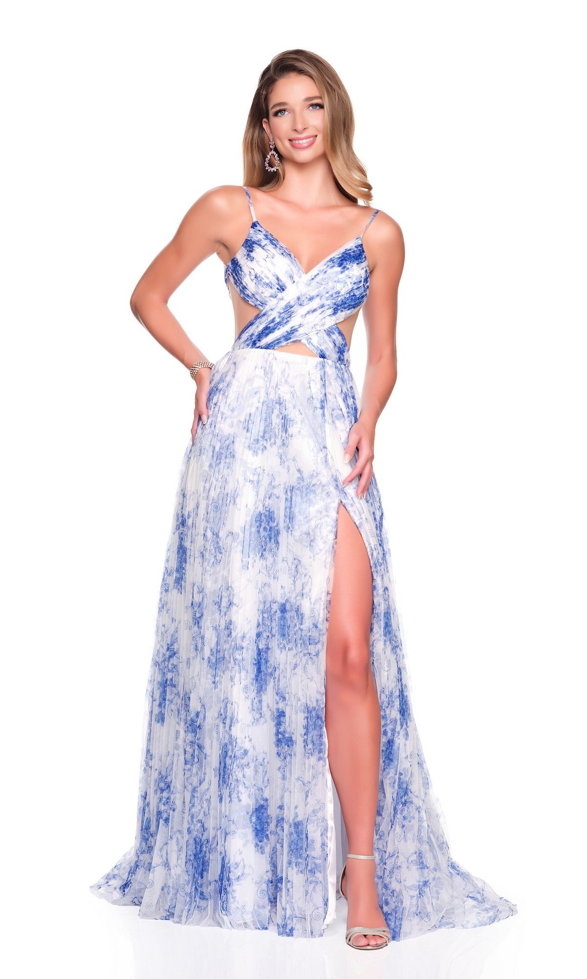 A woman poses and smiles against a white background wearing the Long Prom Dress: Dave and Johnny 12938, a sleeveless chiffon A-line gown featuring a white and blue floral print, floor-length hem, and a high slit.